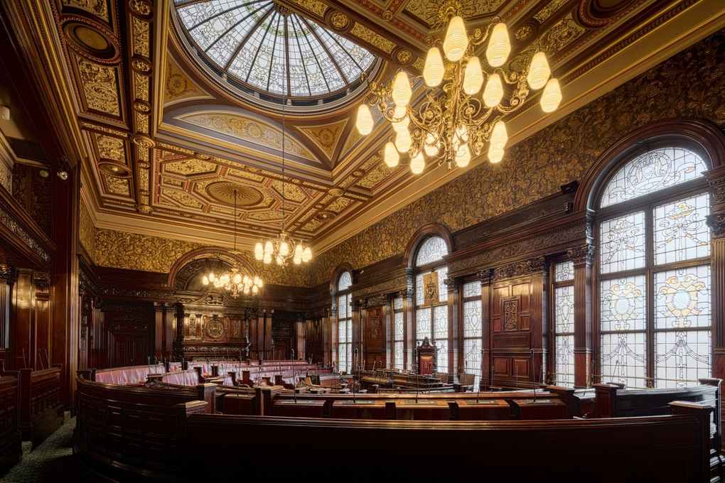 Salle de réunion avec des chandeliers, des bancs, des fenêtres en arc et un plafond décoré Salle de réunion avec des chandeliers, des bancs, des fenêtres en arc et un plafond décoré