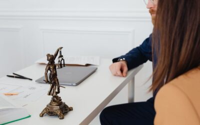 Table blanche avec statue de justice, ordinateur et papiers, deux personnes en conversation