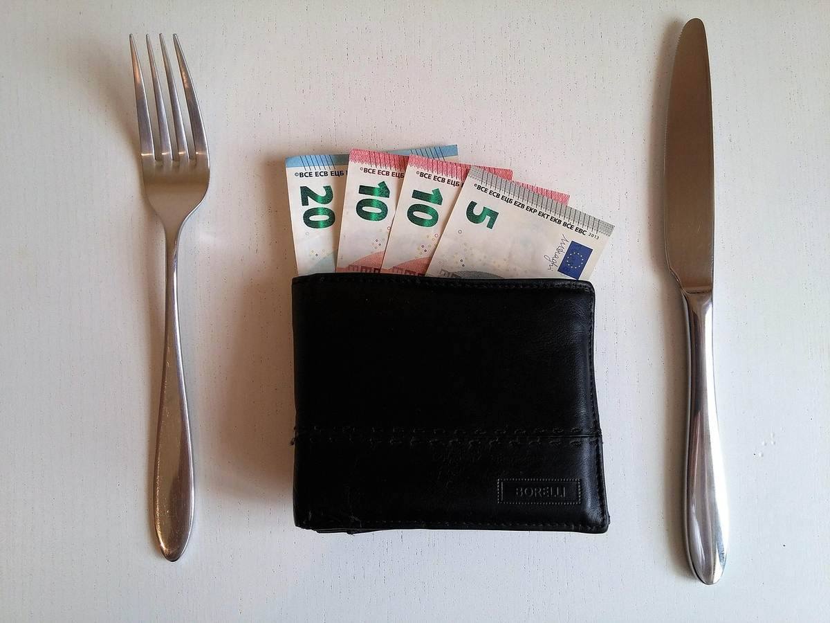 Portefeuille noir avec des billets de 20, 10 et 5 euros entre une fourchette et un couteau sur une table Portefeuille noir avec des billets de 20, 10 et 5 euros entre une fourchette et un couteau sur une table