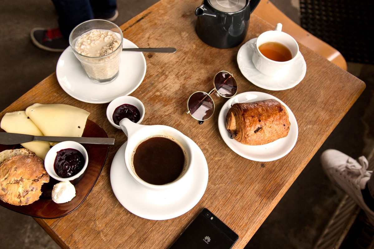 Table en bois avec café, pâtisseries, fromage, thé, téléphone, lunettes, chaussette Table en bois avec café, pâtisseries, fromage, thé, téléphone, lunettes, chaussette