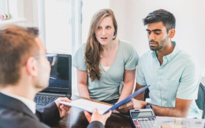 Trois personnes discutant de documents sur un bureau avec ordinateur et calculatrice
