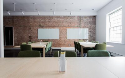 Salle de réunion avec tables blanches, chaises vertes, mur de briques rouges et tableaux blancs