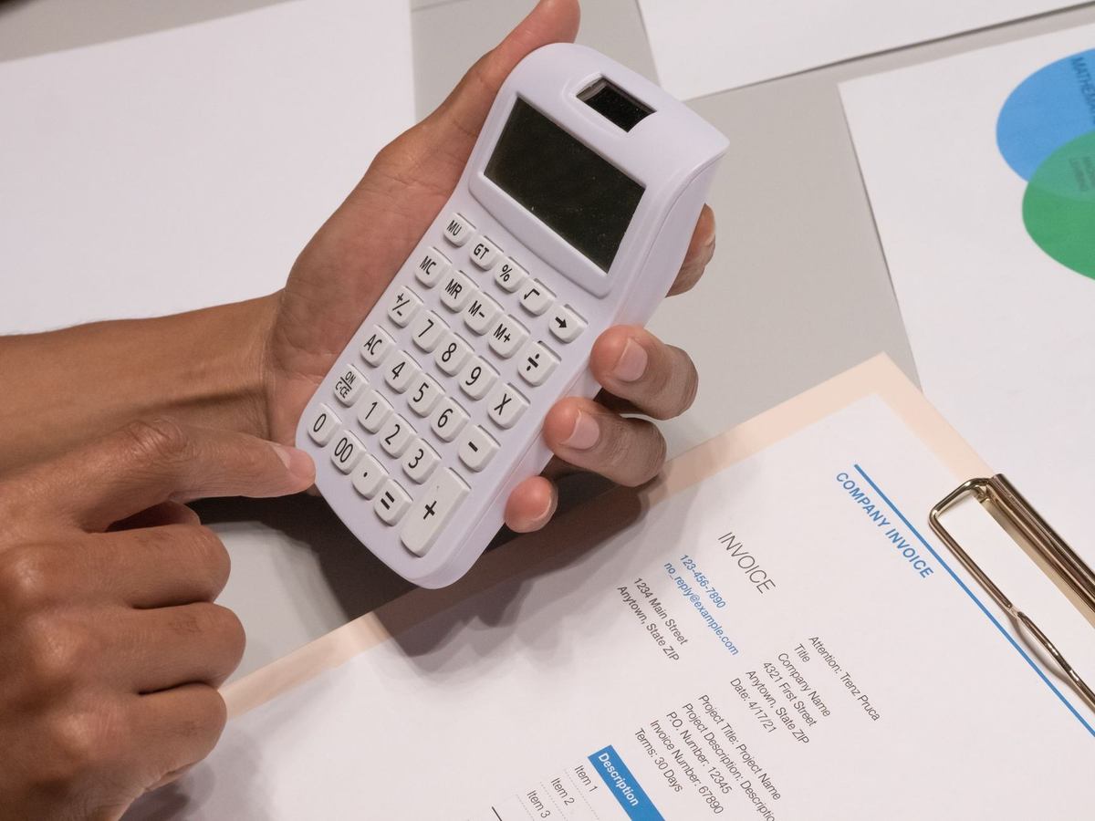 Mains saisissant des chiffres sur une calculatrice, documents et feuilles sur une table